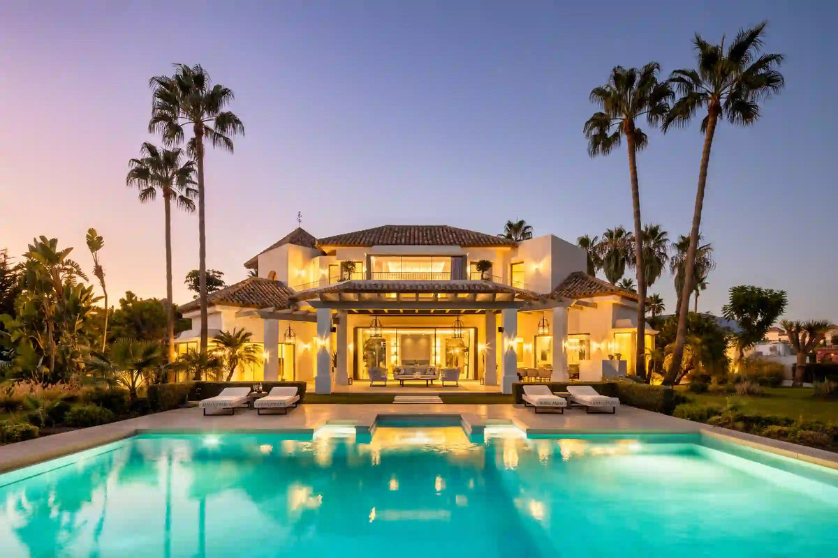 The villa and its pool at dusk, warmly lit from within.