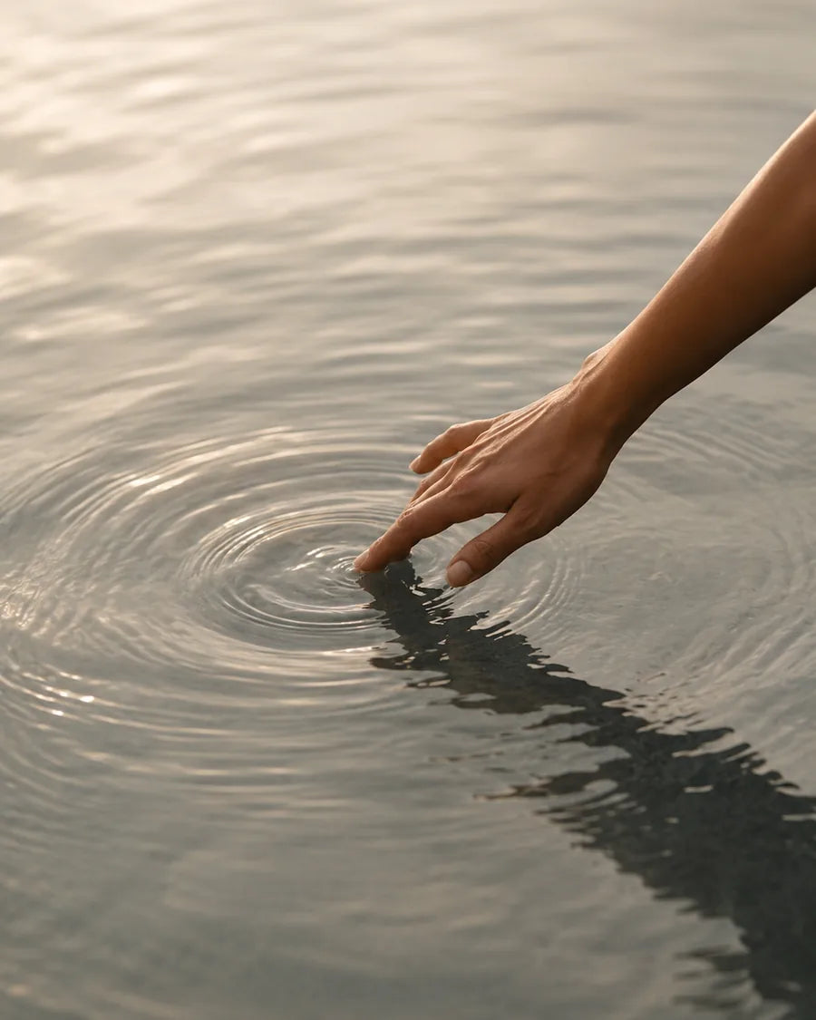 A hand gently touching still water, forming ripples.